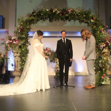 Flahavan/Kurtz Covenant Wedding Whimsical U shaped wedding chuppah adorned with lush greenery, soft fairy lights, and dark purple accent flowers by Remnant Fellowship Wedding Committee